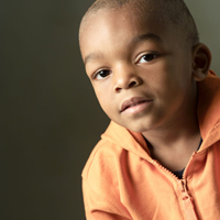 A head and shoulders image of little boy wearing an orange shirt.