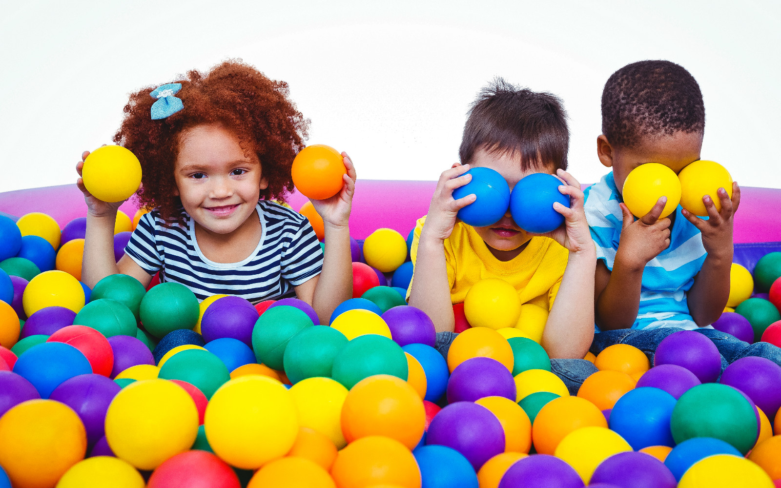 three preschool children holding up sponge balls in a sponge ball pool