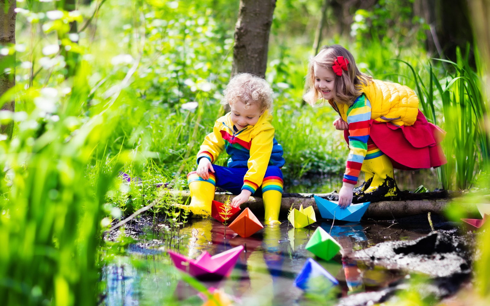 two young children playing with paper boats