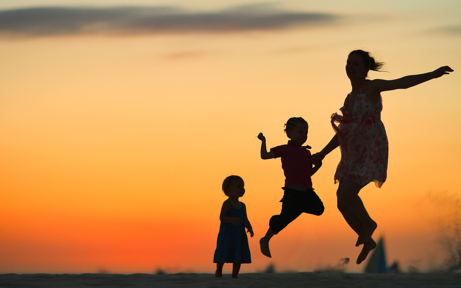 silhouettes of a mother and two young children jumping against the backdrop of the setting sun